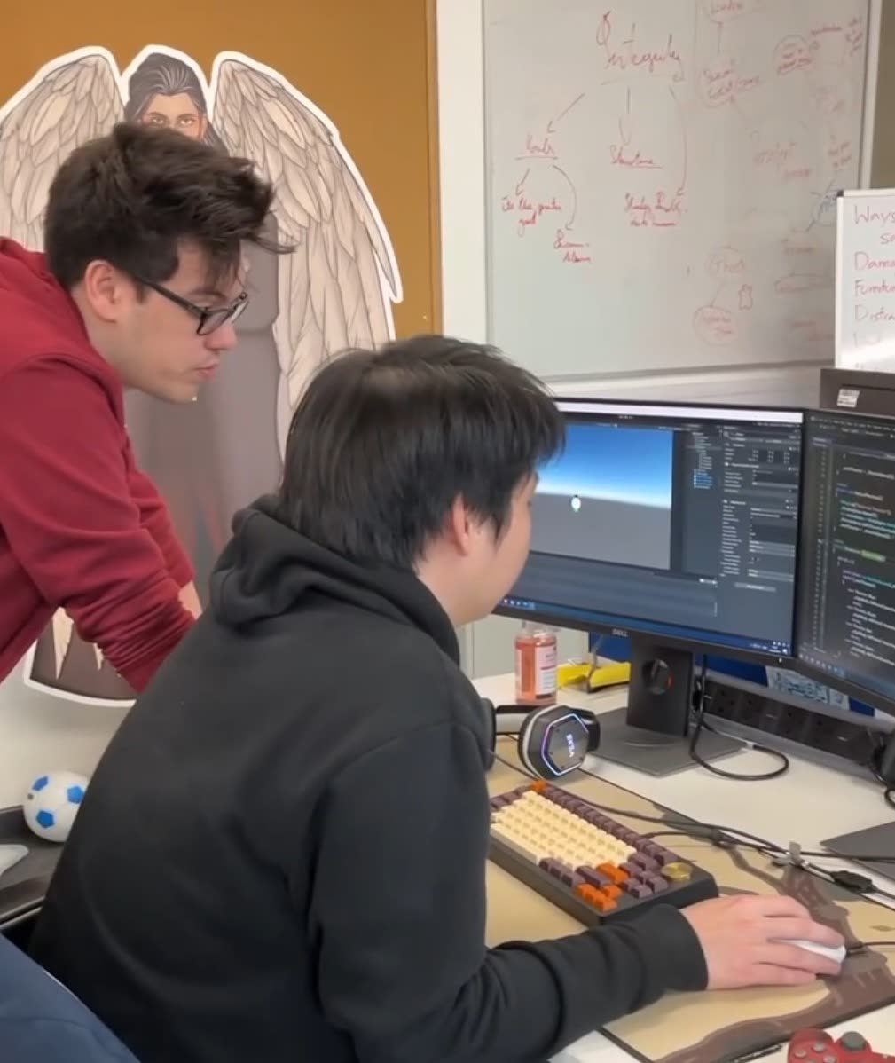 Two students at a workstation reviewing a Unity scene and code side by side.